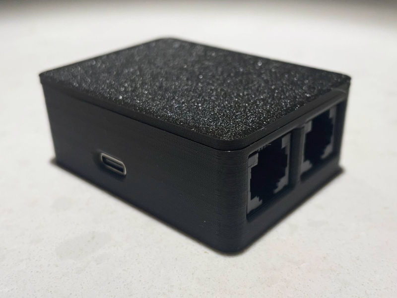 A photo of a small box mounted to the bottom of a desk. Two CAT5 cables are connected to it.